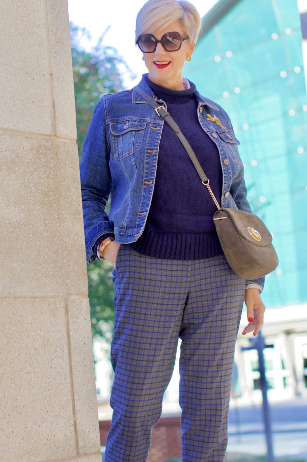 beth from style at a certain age wears a jean jacket, plaid pants, navy blue roll neck sweater, striped shirt, and navy blue loafers