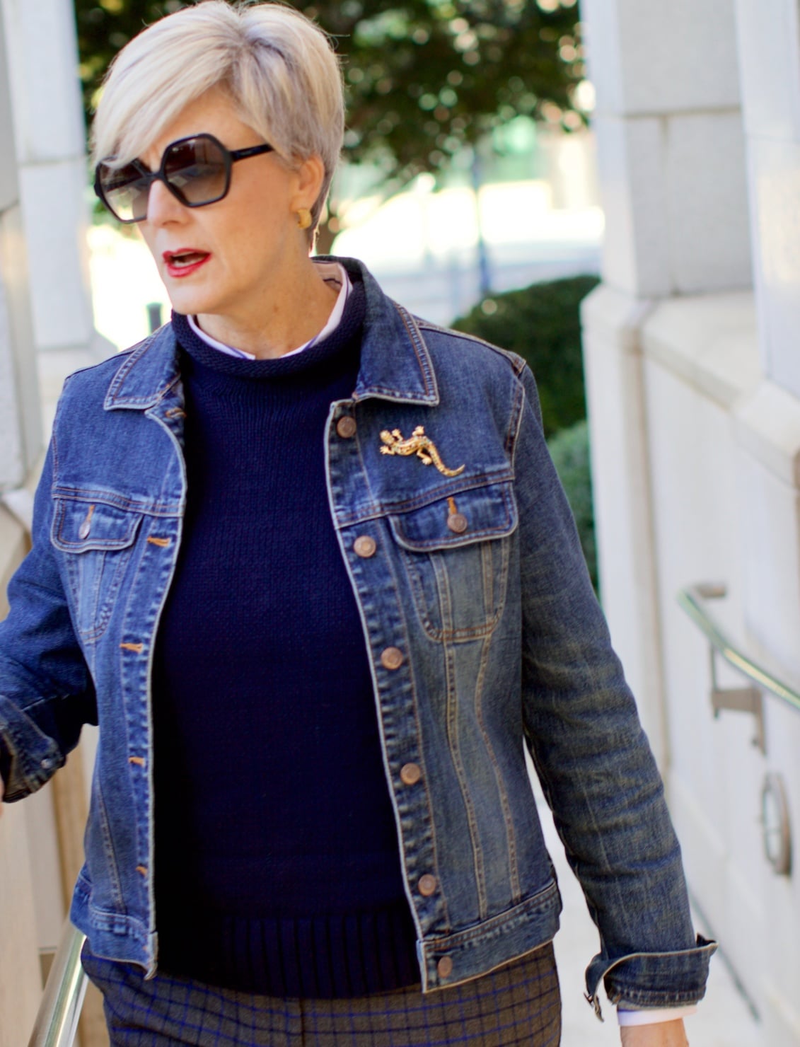 beth from style at a certain age wears a jean jacket, plaid pants, navy blue roll neck sweater, striped shirt, and navy blue loafers