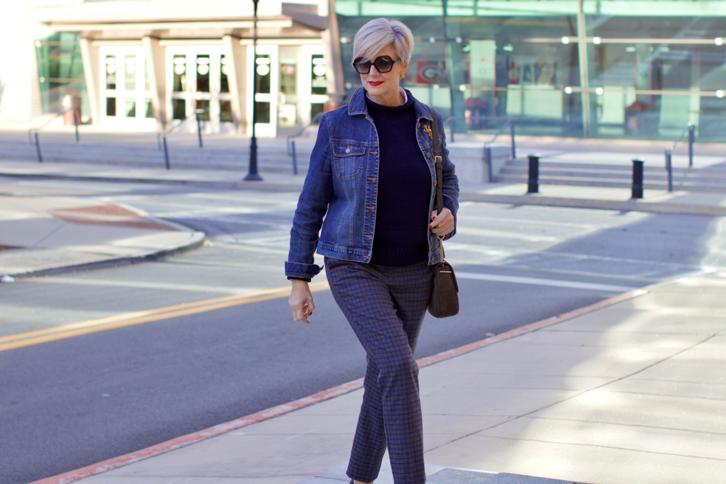 beth from style at a certain age wears a jean jacket, plaid pants, navy blue roll neck sweater, striped shirt, and navy blue loafers