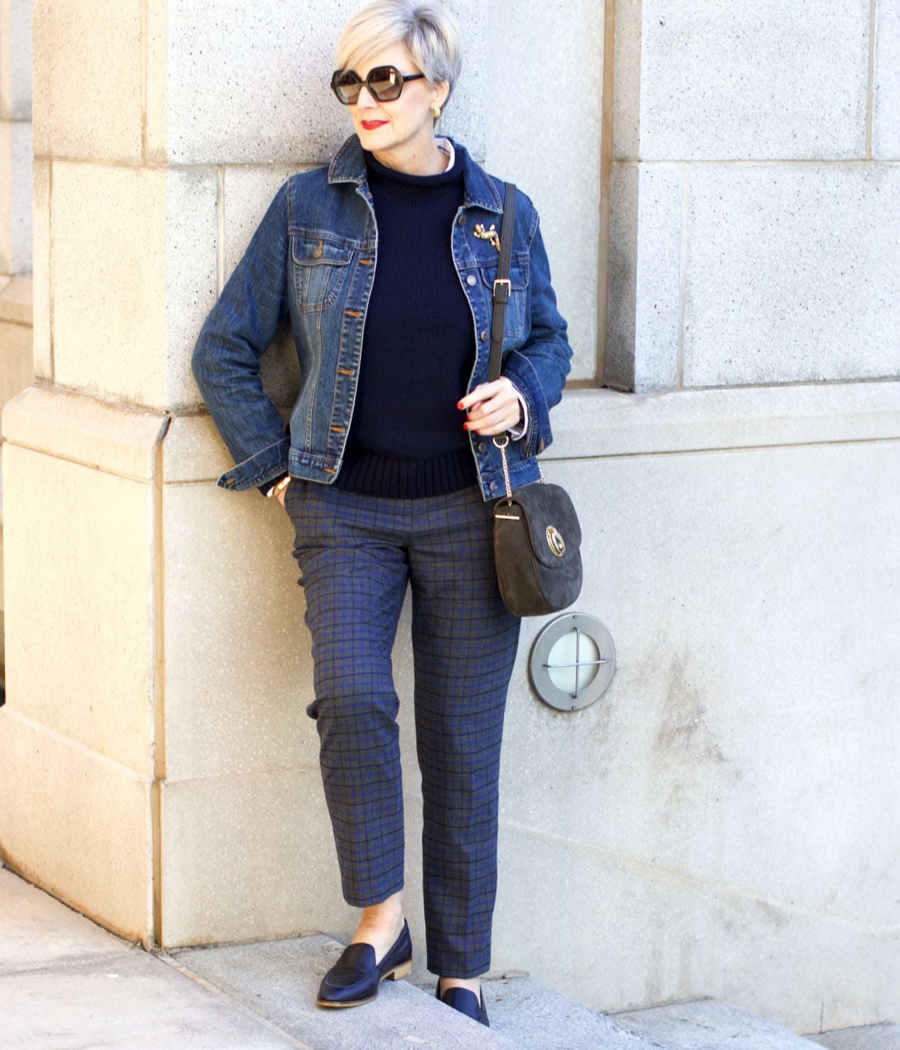 beth from style at a certain age wears a jean jacket, plaid pants, navy blue roll neck sweater, striped shirt, and navy blue loafers