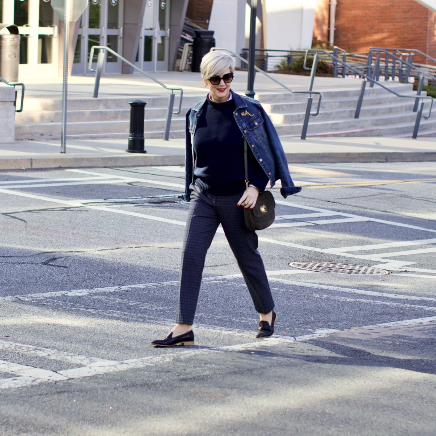 beth from style at a certain age wears a jean jacket, plaid pants, navy blue roll neck sweater, striped shirt, and navy blue loafers