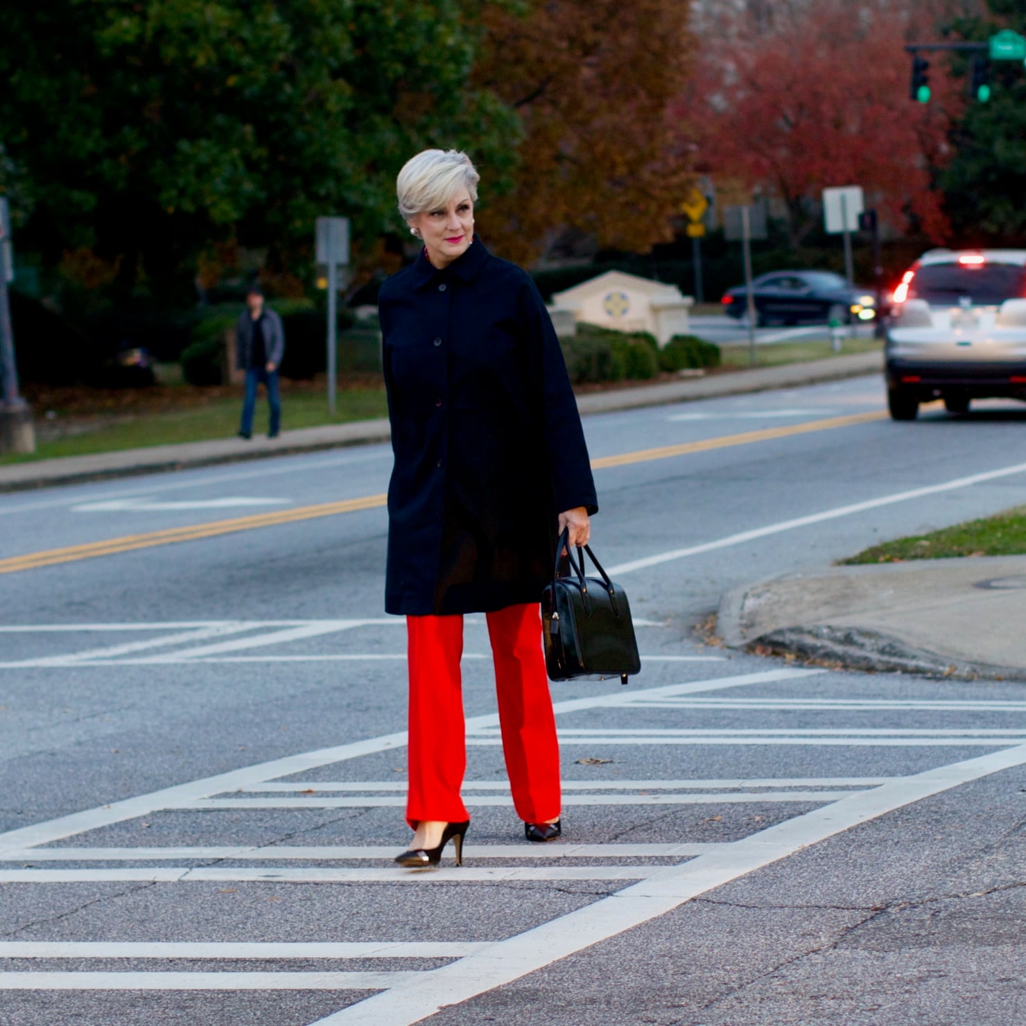 beth from Style at a Certain Age wears Anthropologie red pants, pink and red shirt, Everlane black raincoat, and black suede pumps