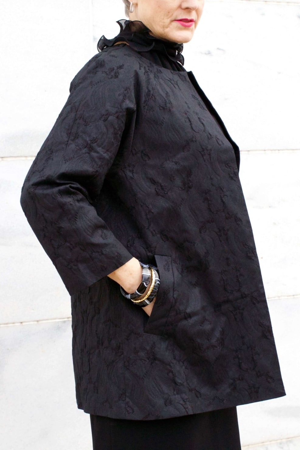 beth from Style at a Certain Age wears a Eileen Fisher shimmer jacquard 3/4 sleeve jacket and ruffled black dress 