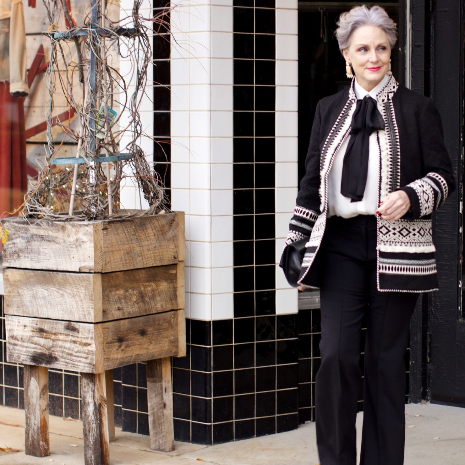 beth from Style at a Certain Age wears black flare pants, bow blouse, embroidered wonderland jacket, and black patent leather pumps