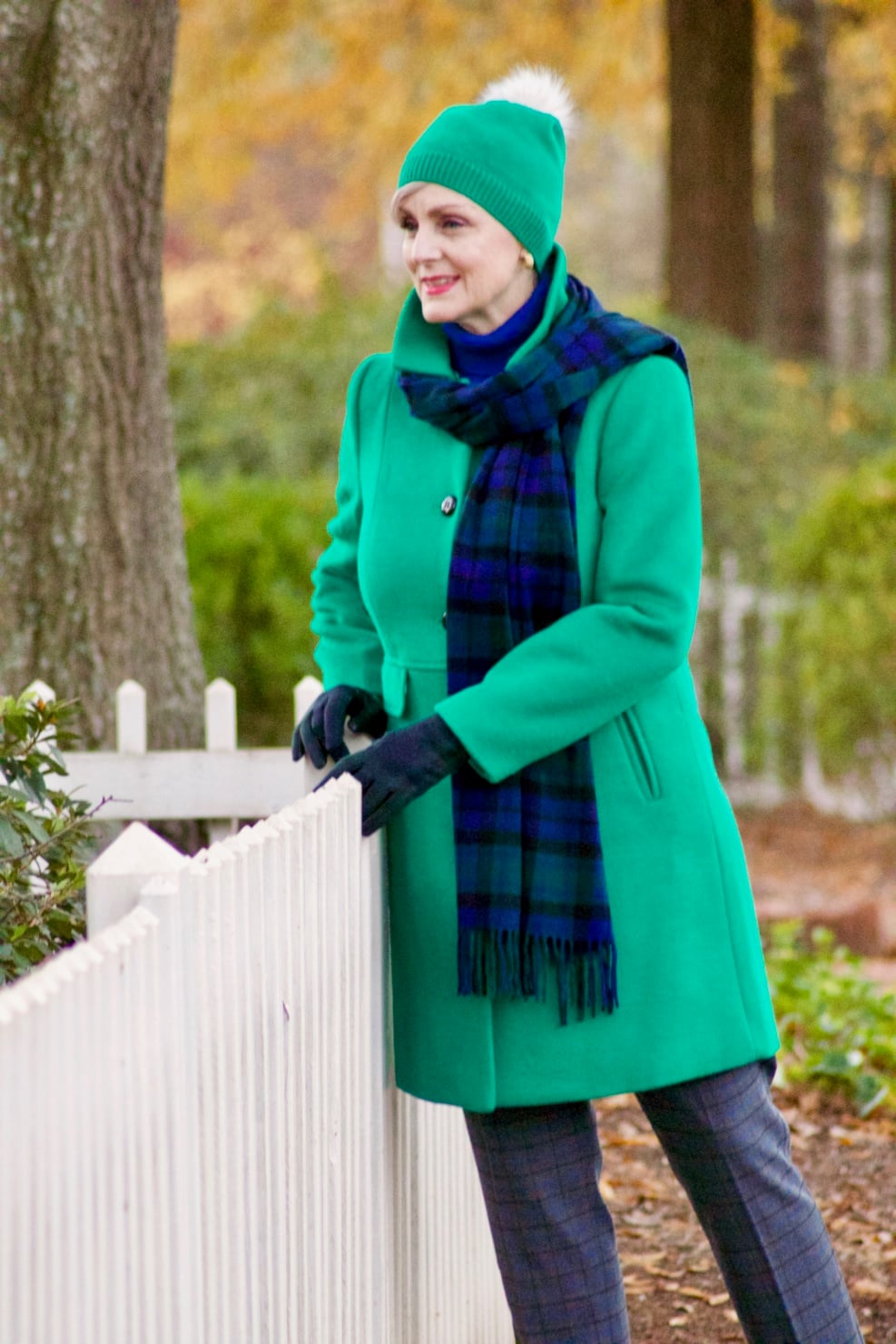 beth from style at a certain age wears plaid pants, cobalt blue turtleneck, green wool coat, blackwatch plaid cashmere scarf, and green beanie