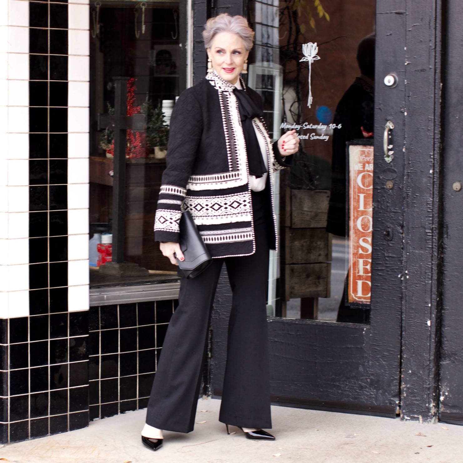 beth from Style at a Certain Age wears black flare pants, bow blouse, embroidered wonderland jacket, and black patent leather pumps