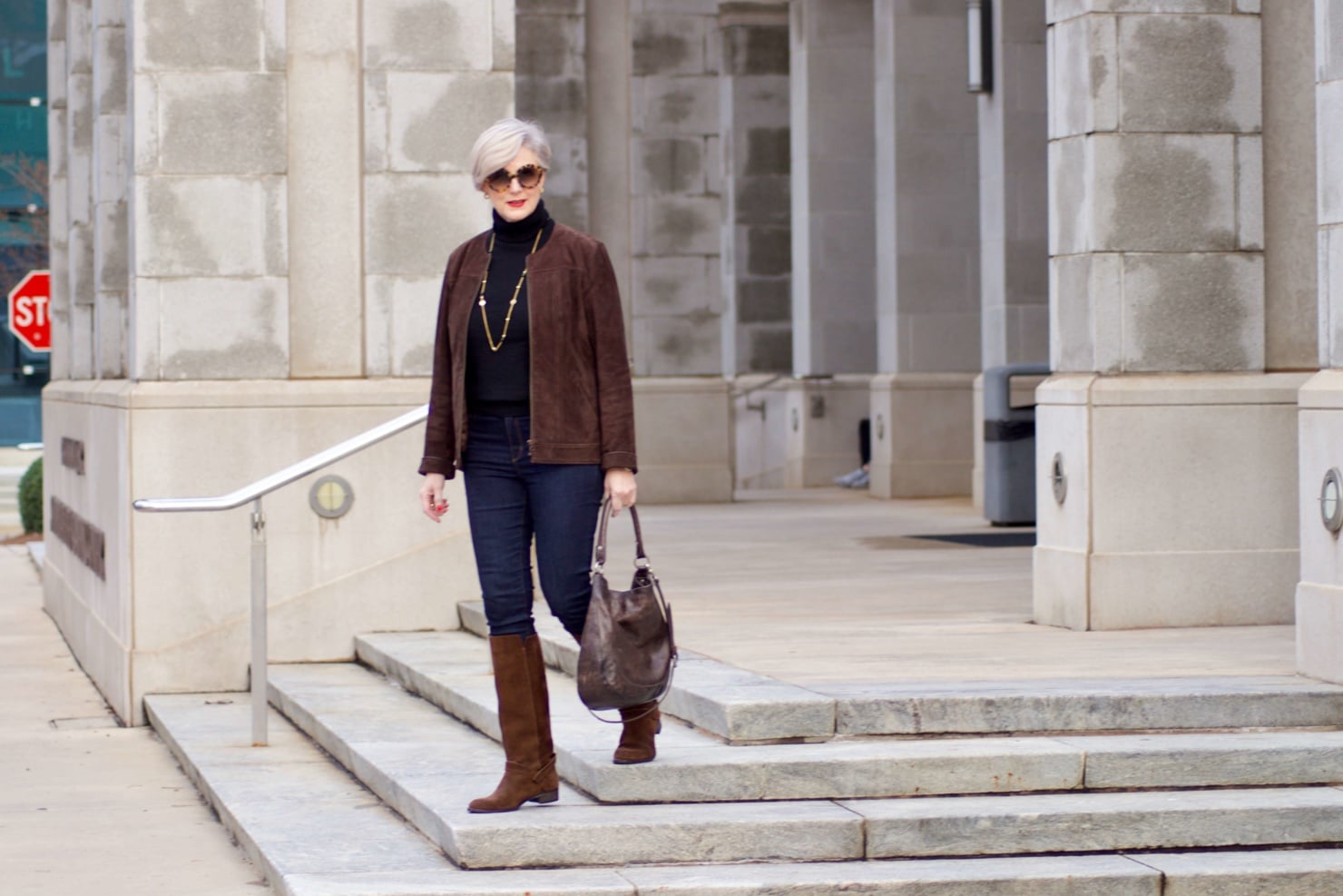 beth from Style at a Certain Age wears a black turtleneck, brown suede jacket, dark rinse denim and suede riding boots