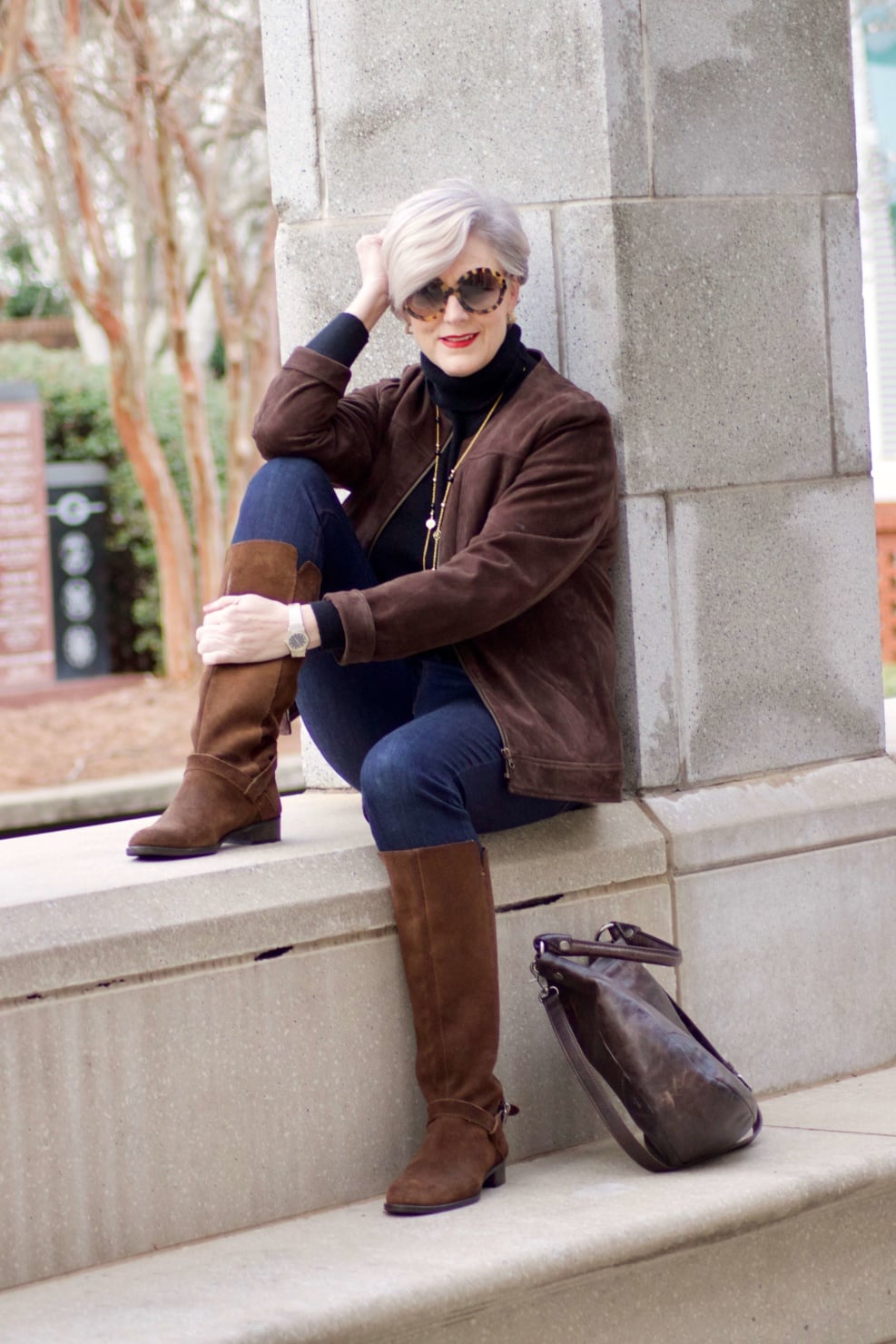 beth from Style at a Certain Age wears a black turtleneck, brown suede jacket, dark rinse denim and suede riding boots