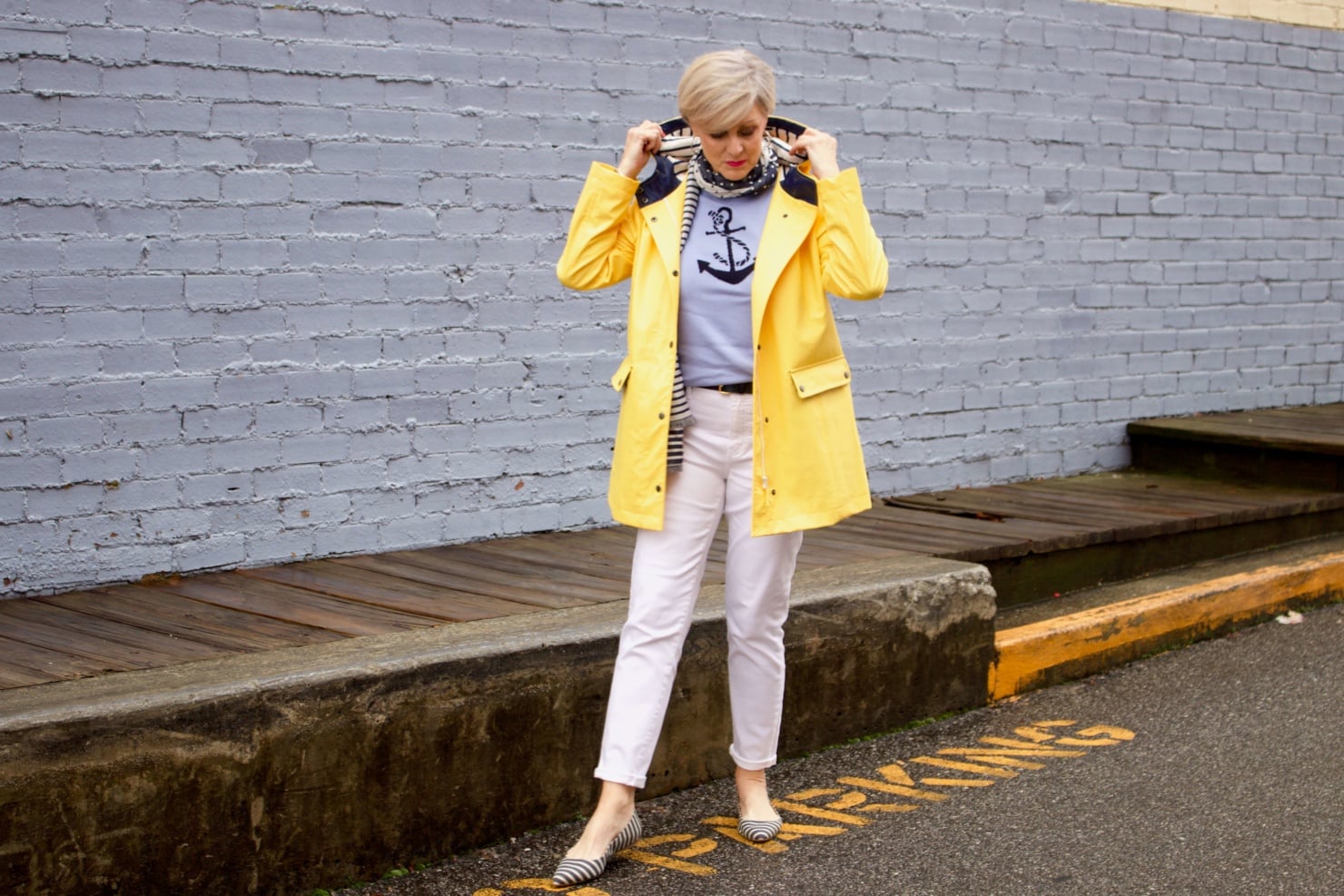 beth from Style at a Certain Age wears a yellow slicker from Talbots, white denim, anchor sweater, polka dot and striped scarf, and striped flats