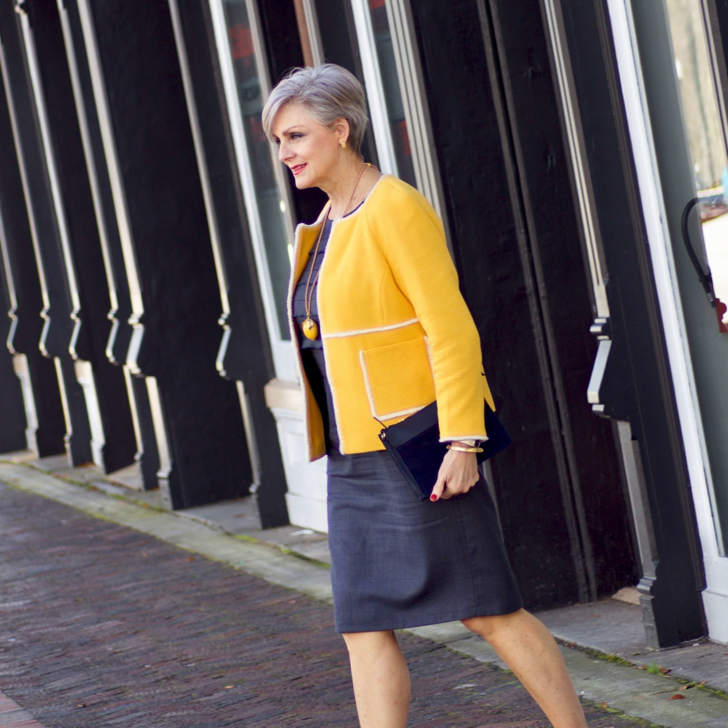 beth from Style at a Certain Age wears a navy blue sheath dress, Boden yellow jacket, navy suede shoes, Tory Burch lemon locket