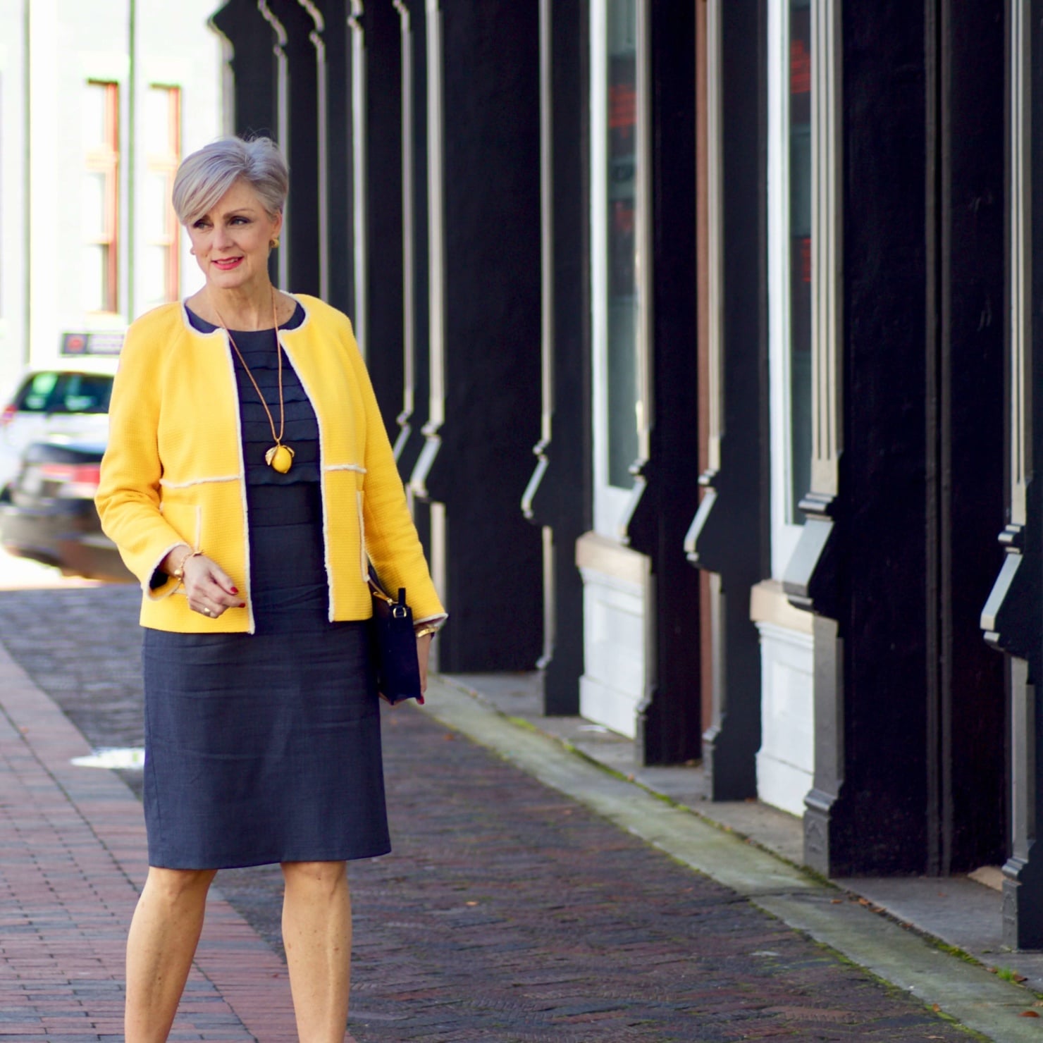 beth from Style at a Certain Age wears a navy blue sheath dress, Boden yellow jacket, navy suede shoes, Tory Burch lemon locket