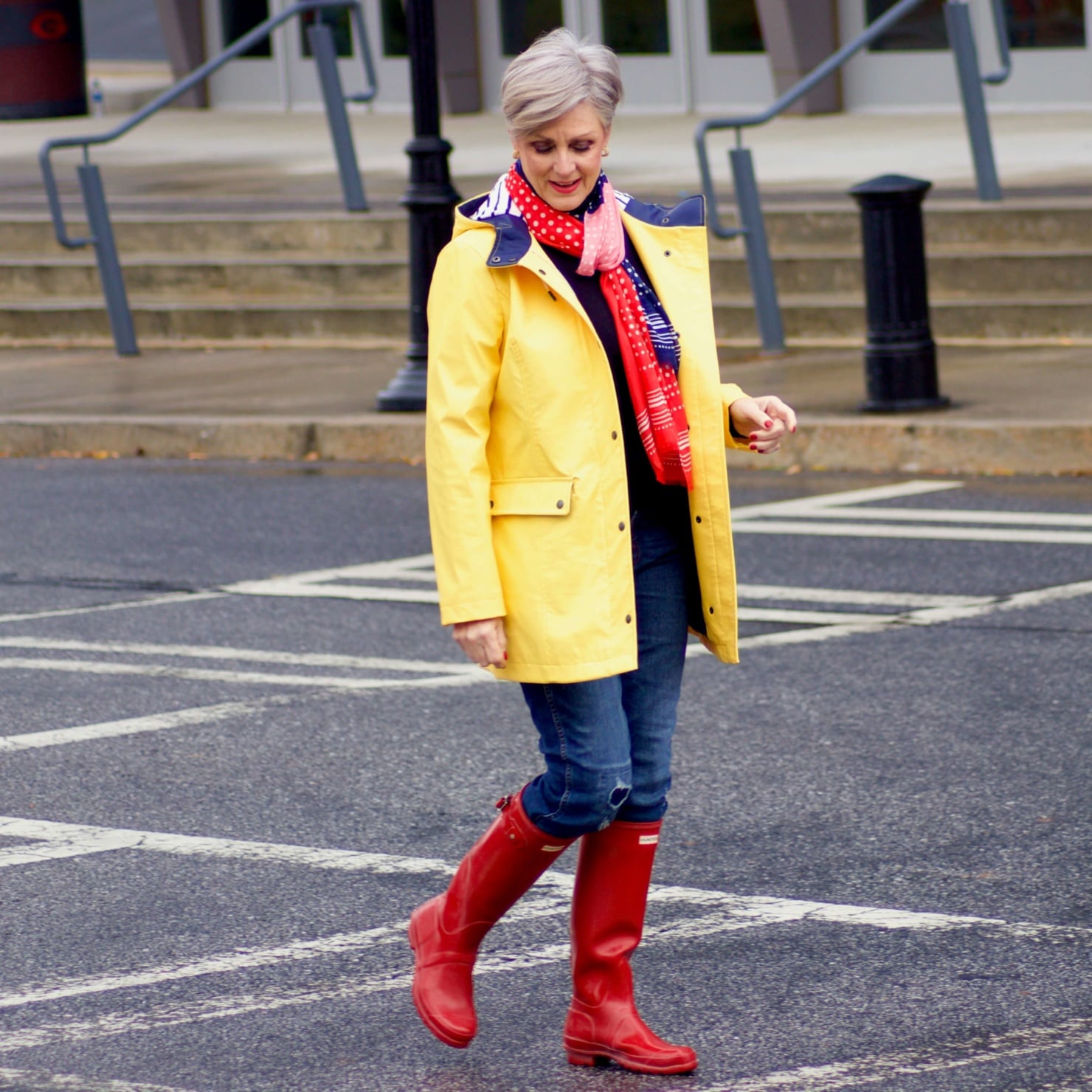 beth from Style at a Certain Age wears Hunter high gloss red rain boots, navy turtleneck, vintage straight jeans, yellow raincoat, and polka dot scarf