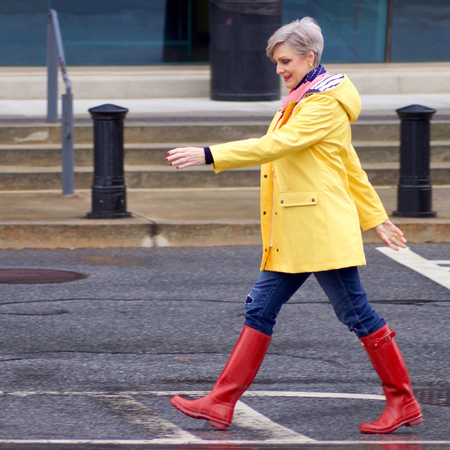 beth from Style at a Certain Age wears Hunter high gloss red rain boots, navy turtleneck, vintage straight jeans, yellow raincoat, and polka dot scarf