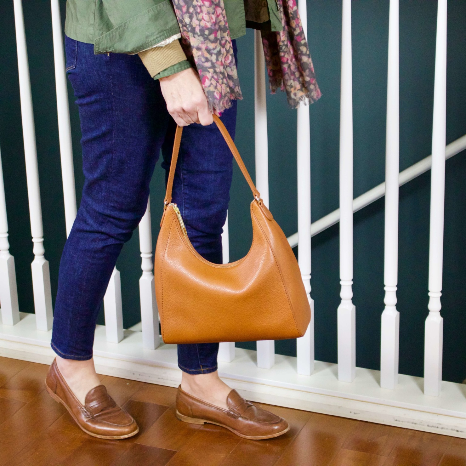 beth from Style at a Certain Age wears a ruffleneck sweater, skinny jeans, green utility jacket, hobo handbag, and loafers