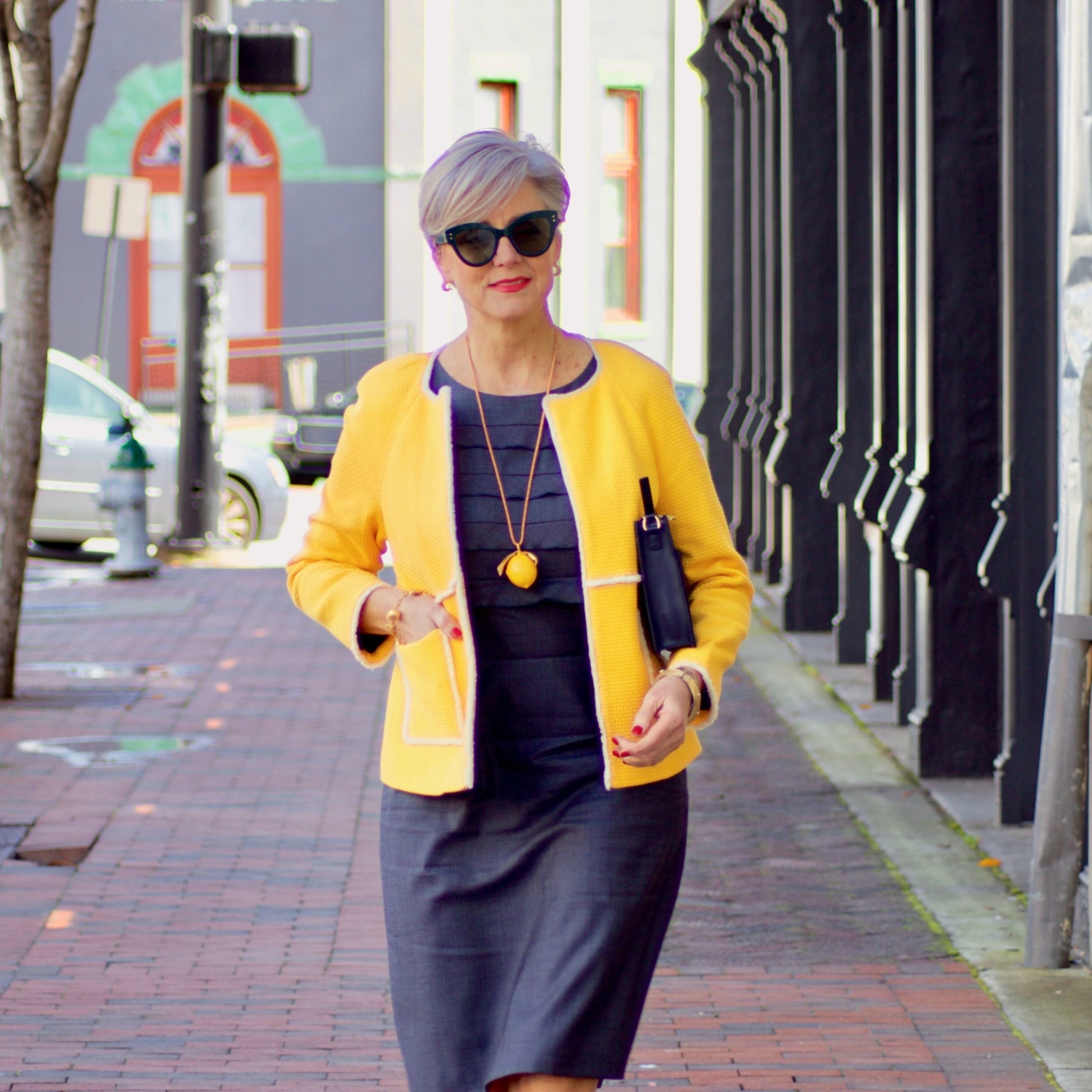 beth from Style at a Certain Age wears a navy blue sheath dress, Boden yellow jacket, navy suede shoes, Tory Burch lemon locket