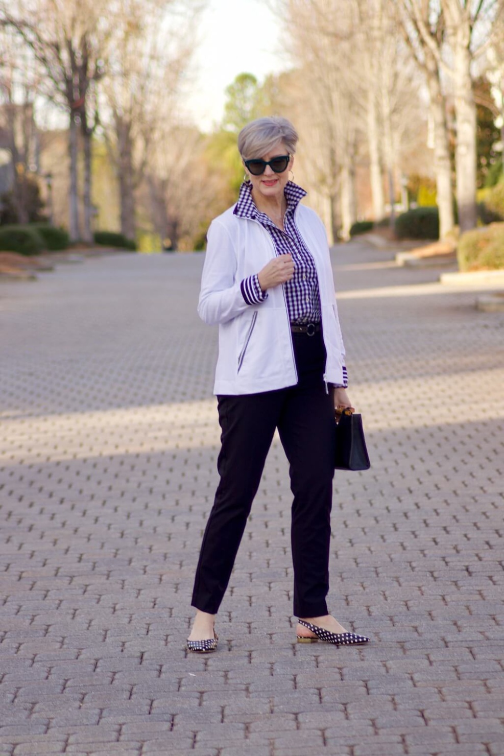 beth from Style at a Certain Age wears a gingham button up, black hampton pants, white track jacket, edison polka dot slingbacks