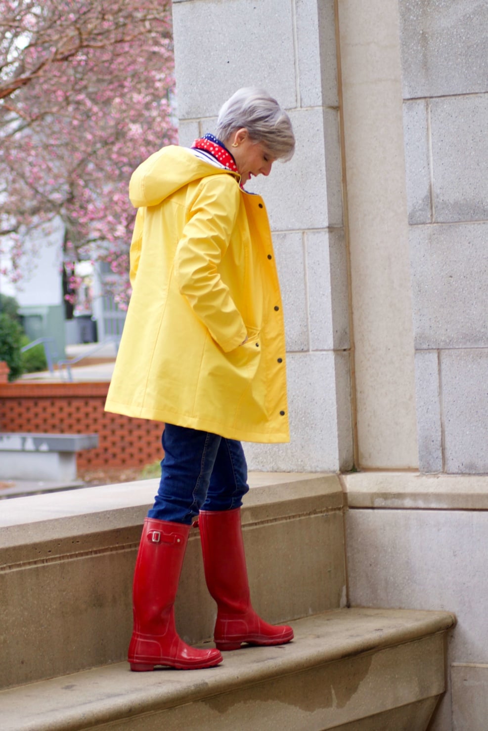 beth from Style at a Certain Age wears Hunter high gloss red rain boots, navy turtleneck, vintage straight jeans, yellow raincoat, and polka dot scarf