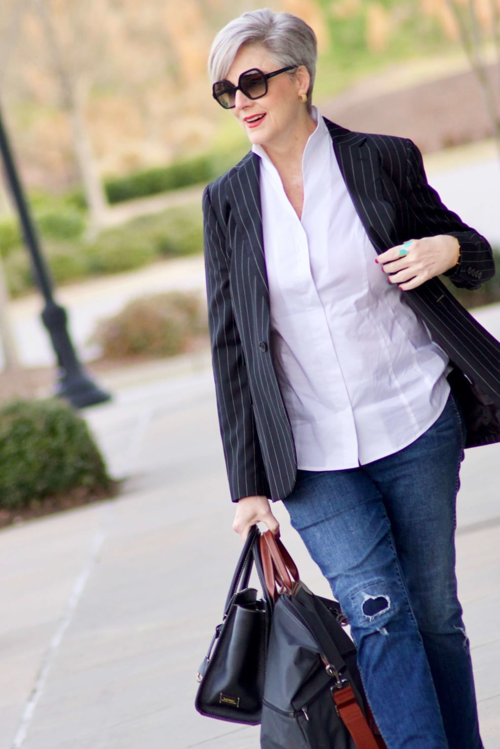 beth from Style at a Certain Age travels in style in a pinstripe blazer, white button down, blue jeans, and black slides