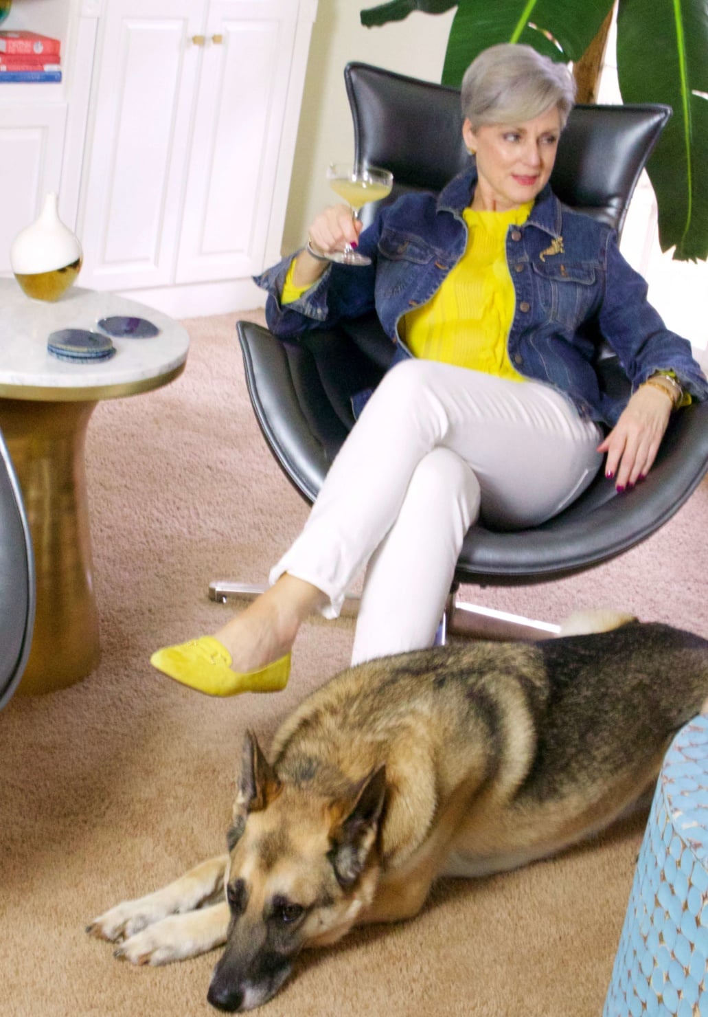 beth from Style at a Certain Age wears a ruffled yellow blouse, white denim, jean jacket, suede driving mocs, and a red camera handbag
