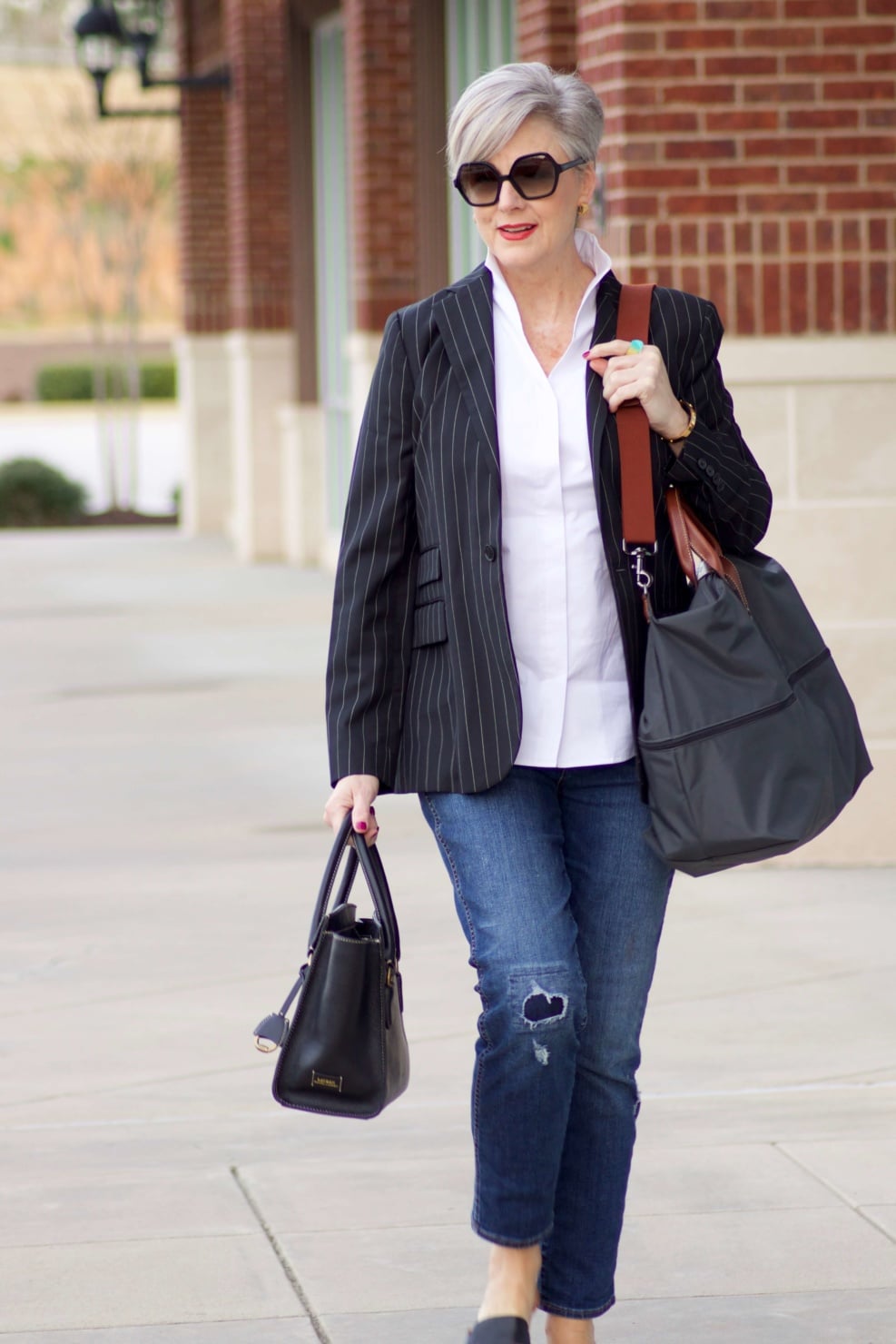 beth from Style at a Certain Age travels in style in a pinstripe blazer, white button down, blue jeans, and black slides