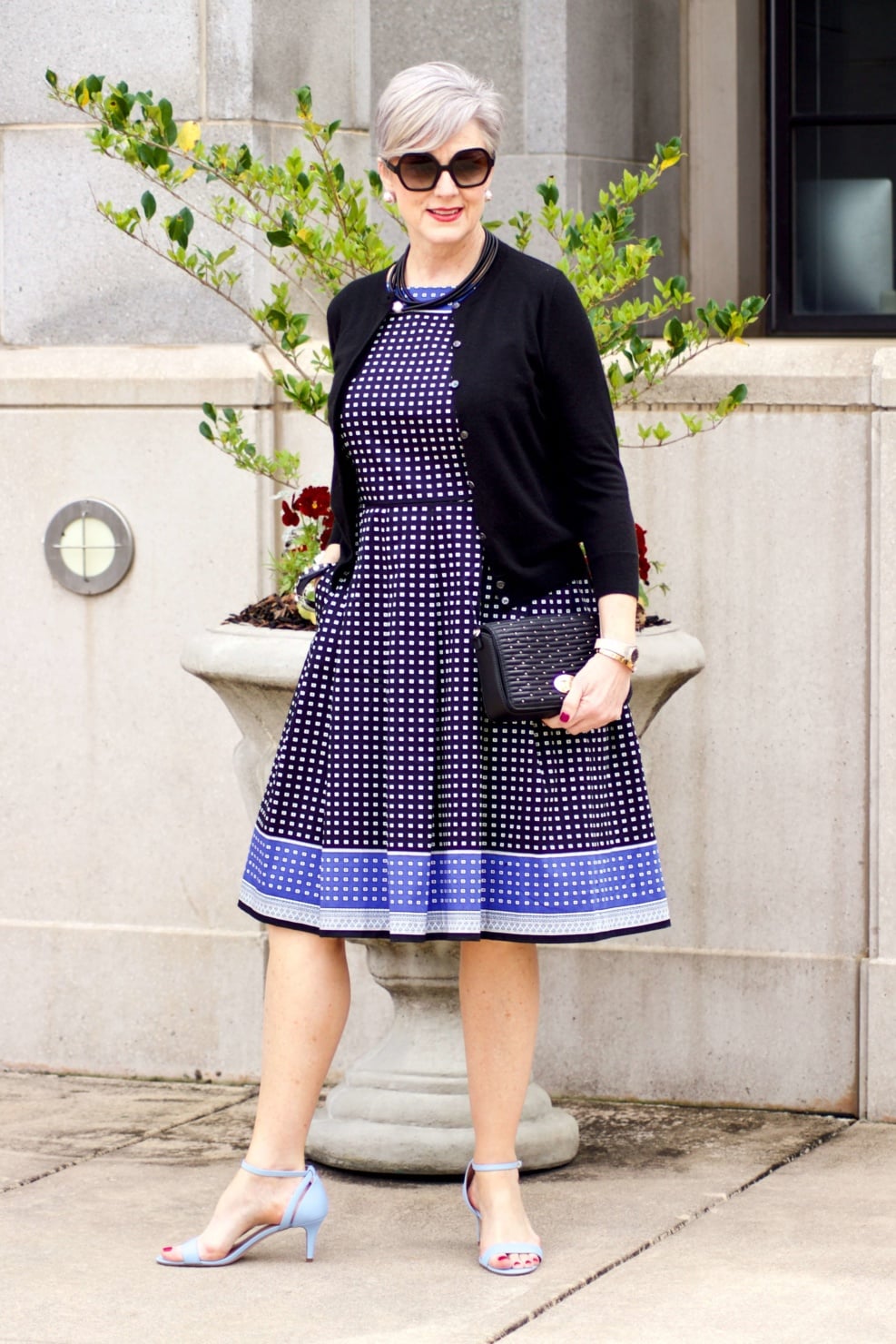 beth from Style at a Certain Age wears a fit and flare dress, kitten heel sandals, and a black clutch handbag