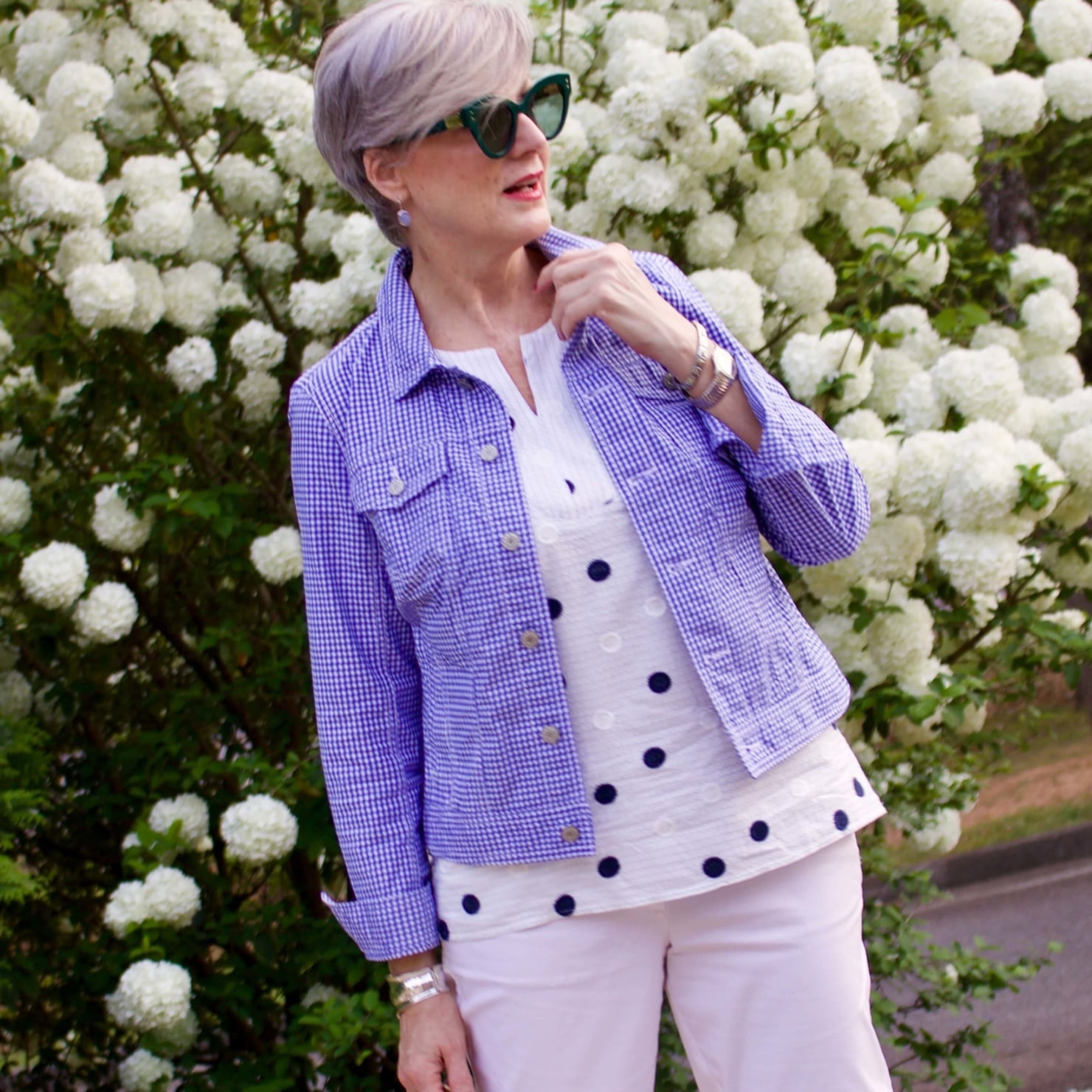 beth from Style at a Certain Age wears a gingham jean jacket, polka dot top, white chinos and wicker handbag