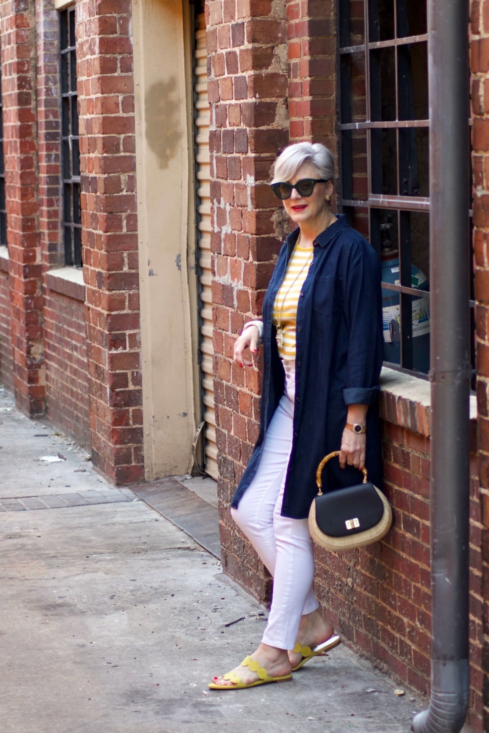 beth from Style at a Certain Age wears a denim duster, striped tee, white denim, suede sandals and wicker handbag