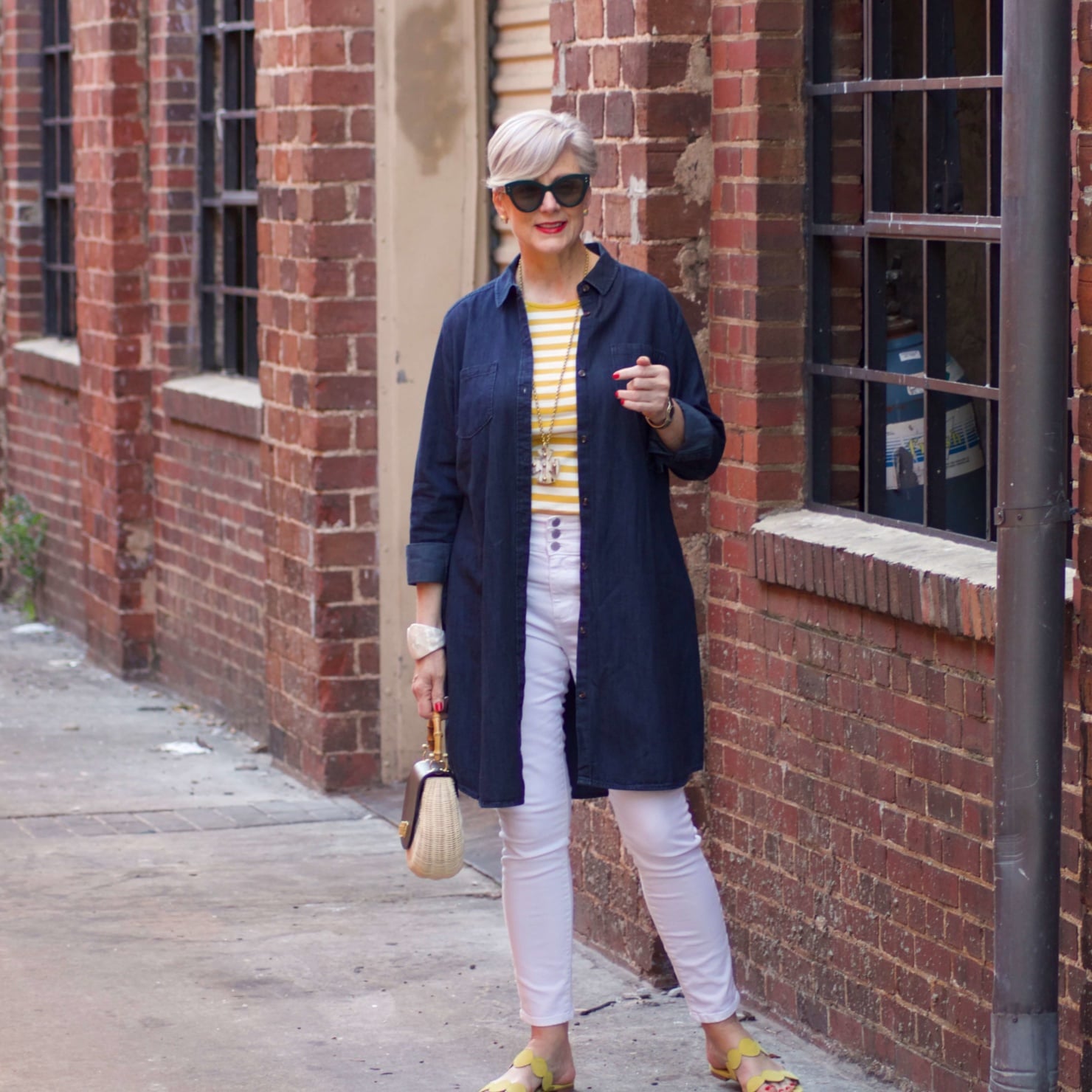 beth from Style at a Certain Age wears a denim duster, striped tee, white denim, suede sandals and wicker handbag