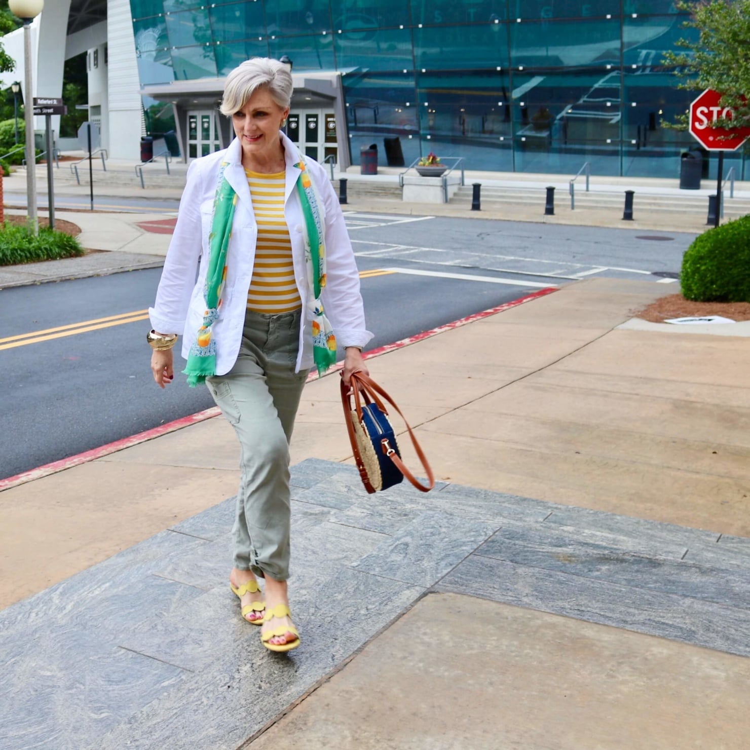 how to wear a jacket for spring and summer beth from Style at a Certain Age wears a white utility jacket, striped tee, green utility pants, yellow sandals, lemon scarf, and cornhusk handbag