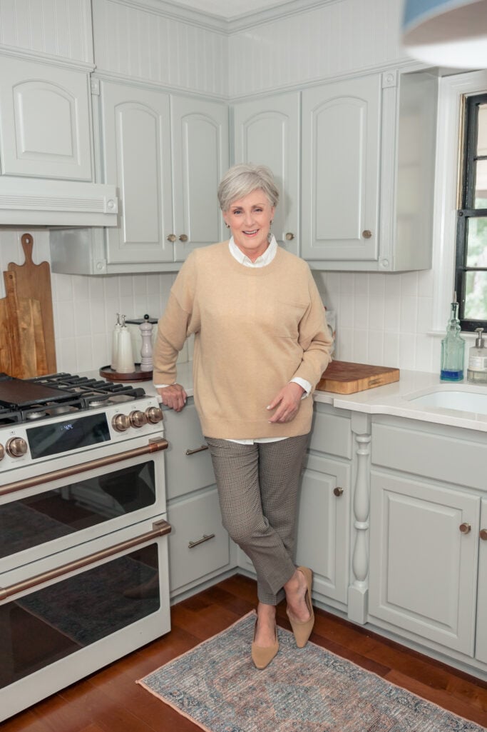 Beth standing in remodeled kitchen with Coventry Gray cabinets, Café Elite dual oven range, and Calcutta Gold Silestone countertops — timeless 2025 remodel.