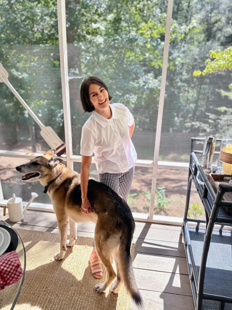 Kelly in white shirt and gingham shorts with Oscar the German Shepherd on screened porch - Fridays with Oscar April 2024