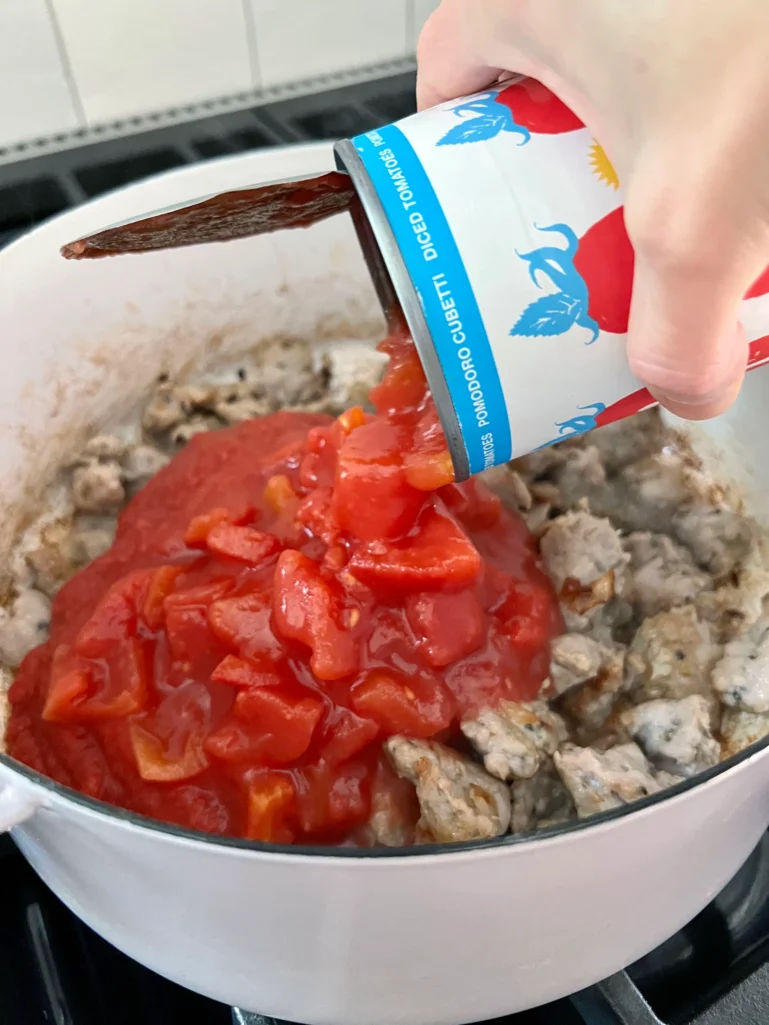 adding the diced tomatoes to the sausage for the lasagna sauce