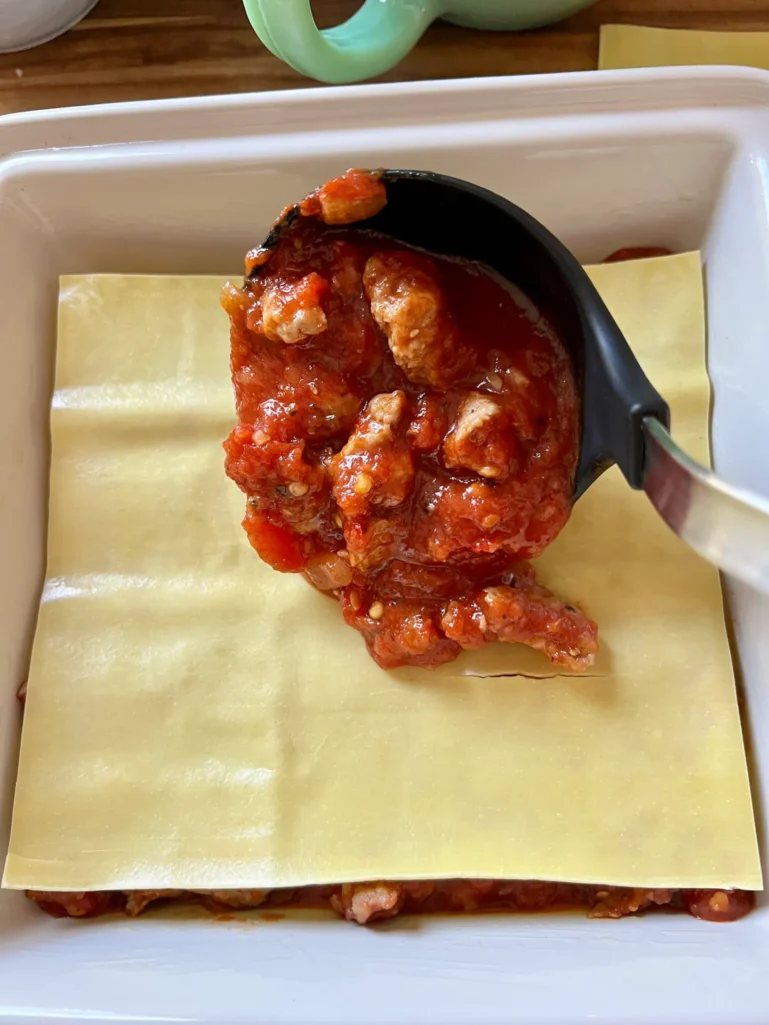 ladling sausage and tomato sauce on lasagna noodles