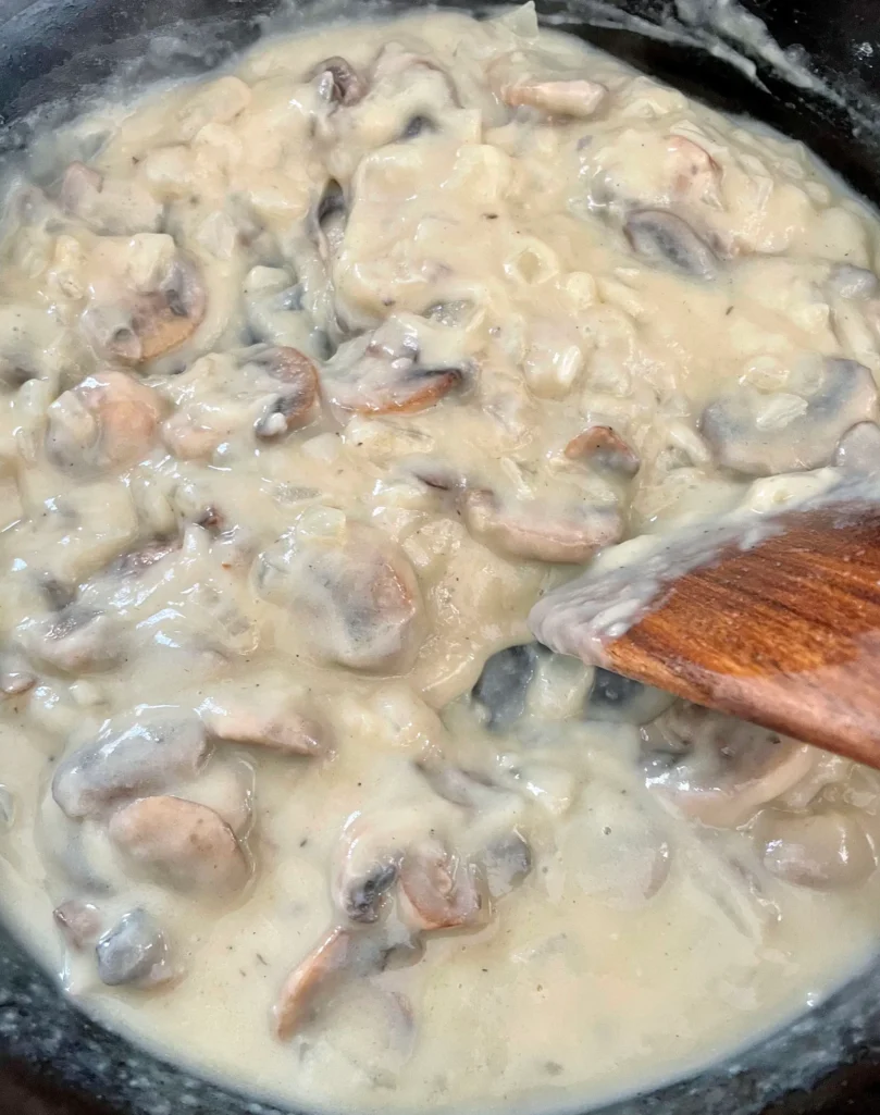 Thick, creamy mushroom and onion gravy being stirred with a wooden spoon in a cast iron skillet