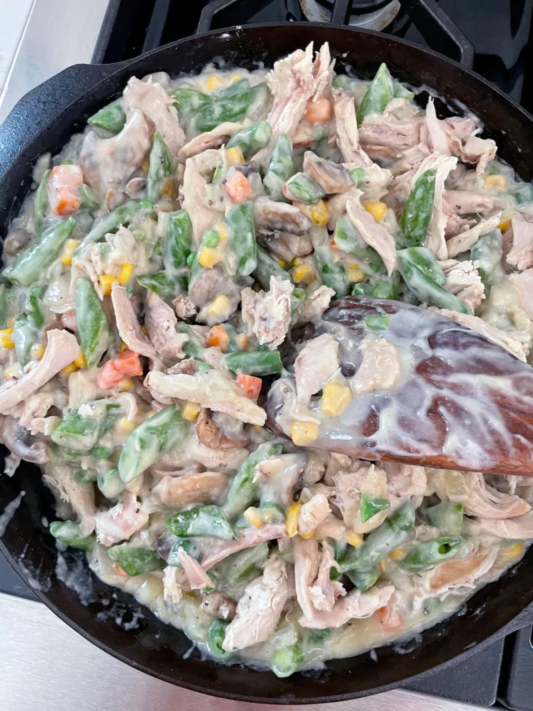 Finished pot pie filling with shredded chicken, mixed vegetables, mushrooms, and cream sauce all stirred together in a cast iron skillet