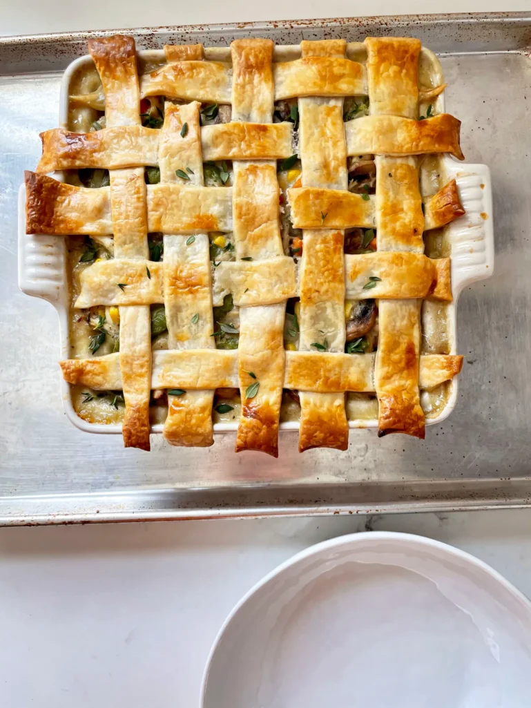 Overhead view of freshly baked golden brown lattice crust on spring chicken pot pie in a white casserole dish on a sheet pan, garnished with fresh thyme