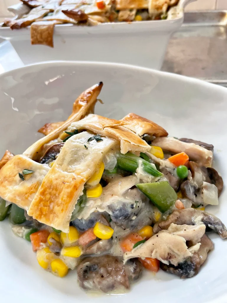 Angled view of a serving of spring chicken pot pie in a white bowl with the baked casserole dish visible in the background