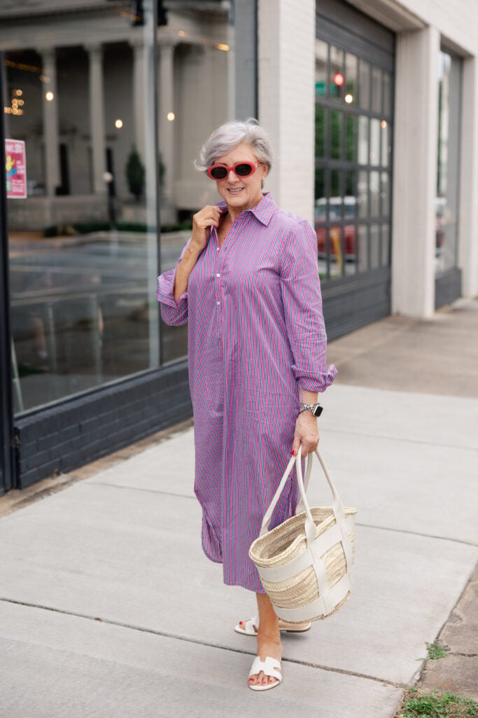 Beth wears a blue-and-red striped poplin dress with white sandals and a straw bag—a summer outfit formula that flatters women over 50