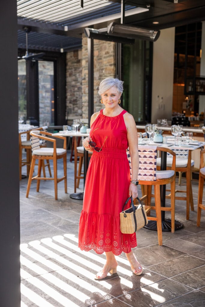 Elegant woman over 50 in red halter dress with straw bag and gold hoop earrings
