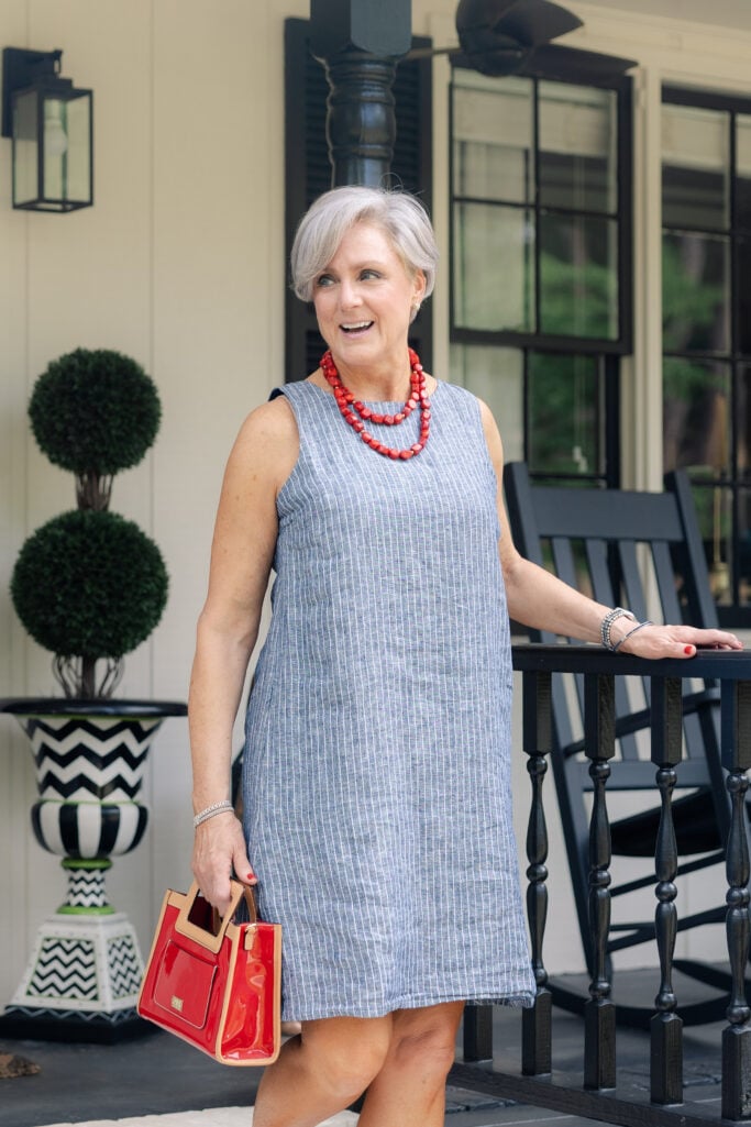 Woman over 50 in striped linen dress with red bead necklace and red handbag