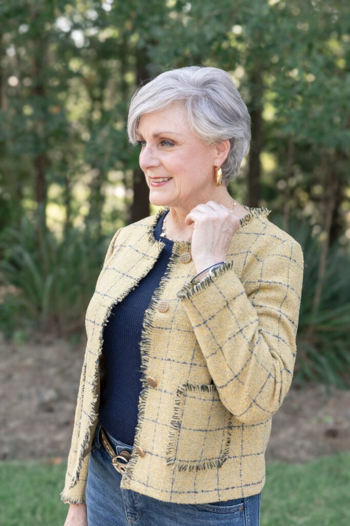 Chic fall outfit for women over 50 featuring a tailored yellow check blazer, cuffed jeans, gold shoes, and a structured handbag.