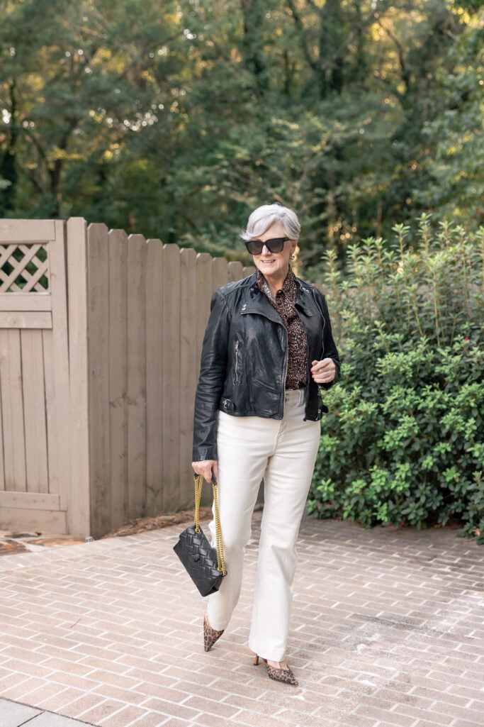 Beth Djalali wears black leather jacket, leopard print blouse, and ivory jeans—an edgy, elegant fall outfit idea.