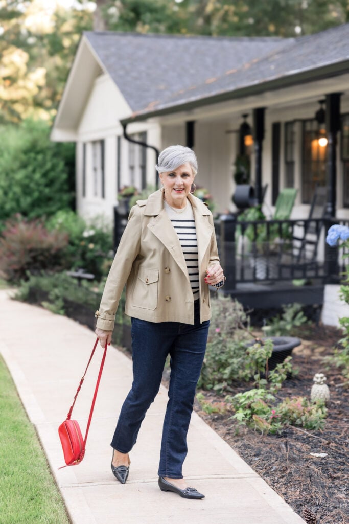 Beth Djalali in tan trench coat, striped sweater, and dark jeans with red crossbody bag—classic Parisian fall outfit.
