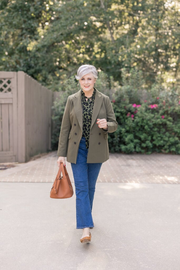 Woman over 50 wearing dark jeans and an olive blazer.