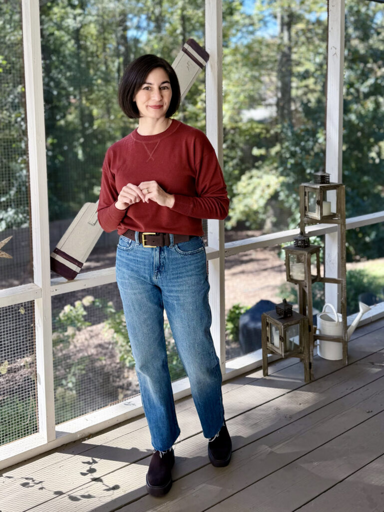 Kelly wearing a rust crewneck sweatshirt with rigid straight-leg jeans, a suede belt, and chunky Chelsea boots — casual fall weekend outfit for petites.