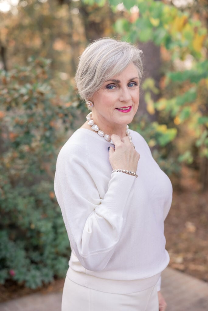 Over 50 woman wearing a white sweater styled with pearl jewelry