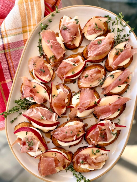 A platter of pear and prosciutto crostini with creamy cheese, fresh thyme, and a drizzle of balsamic glaze, perfect for cozy fall entertaining.