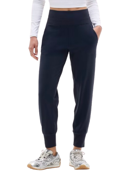 Navy Athleta Venice Joggers featuring a wide high-rise waistband, slim tapered legs with cuffed hems, and side pockets, shown on a model wearing a white long-sleeve top and metallic sneakers.