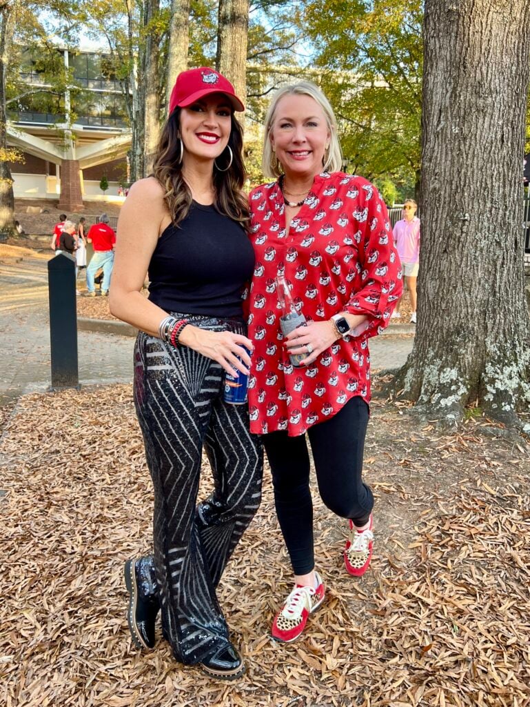 Two women at UGA football tailgate wearing red Georgia gear, one in black sequin palazzo pants with UGA cap