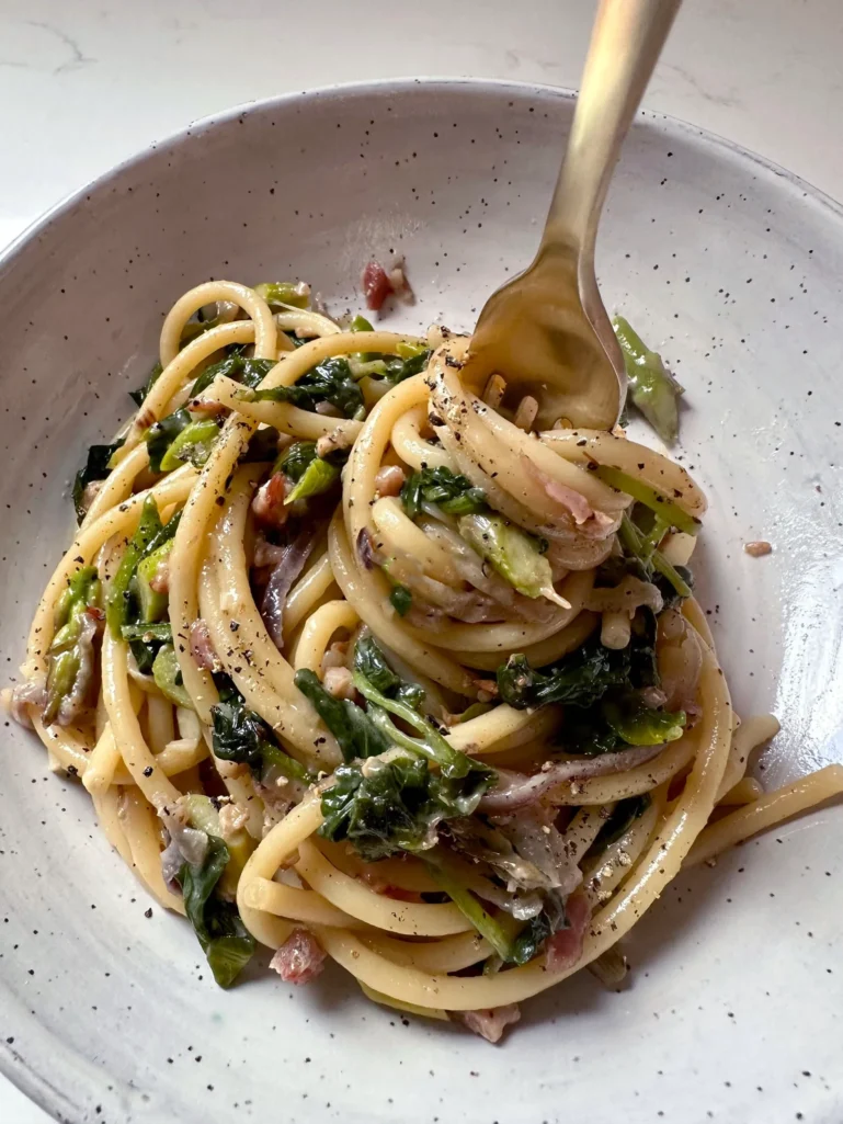 Fork twirling creamy blue cheese bucatini with asparagus and kale in speckled bowl